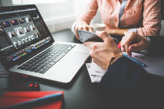 Two people sitting at a table with a laptop and phone.