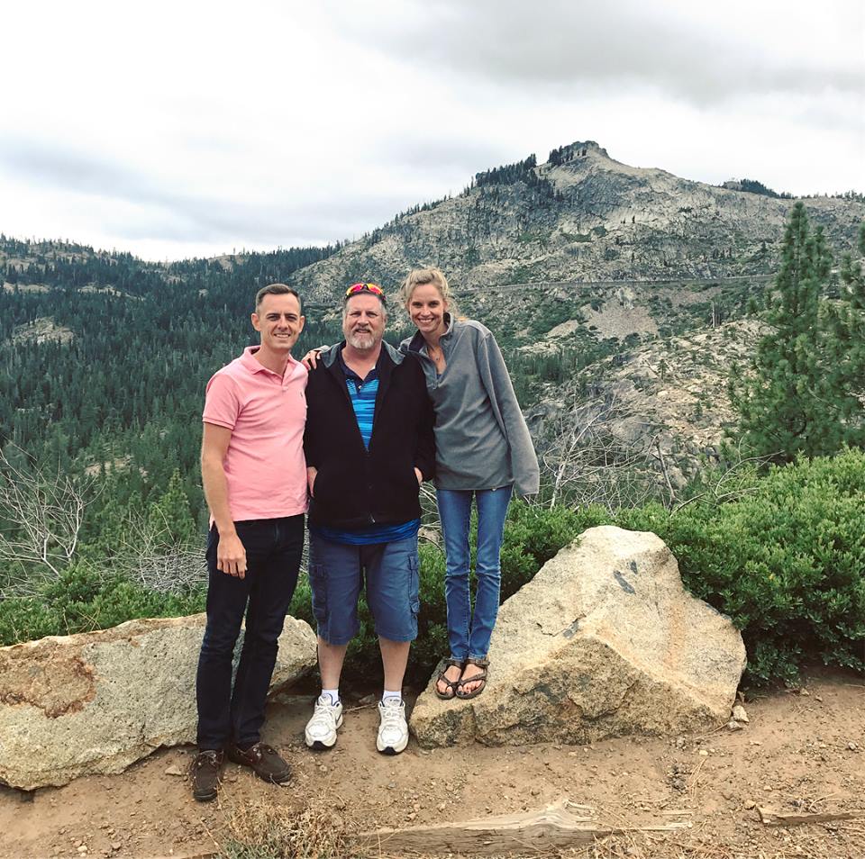 Three women standing on a rock formation near some trees.