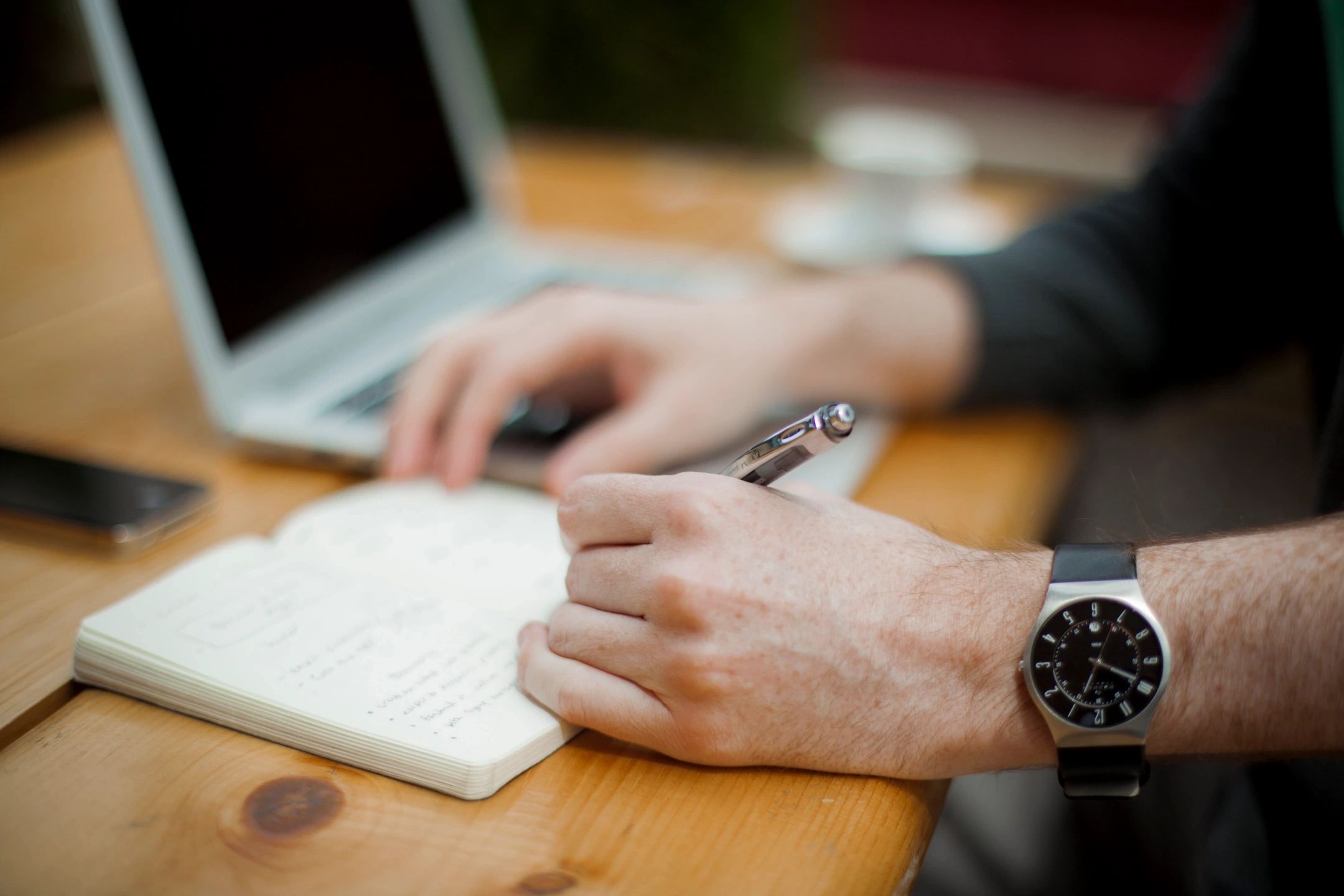 A person is writing on paper with a laptop.