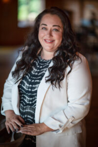 A woman in white jacket standing next to a table.